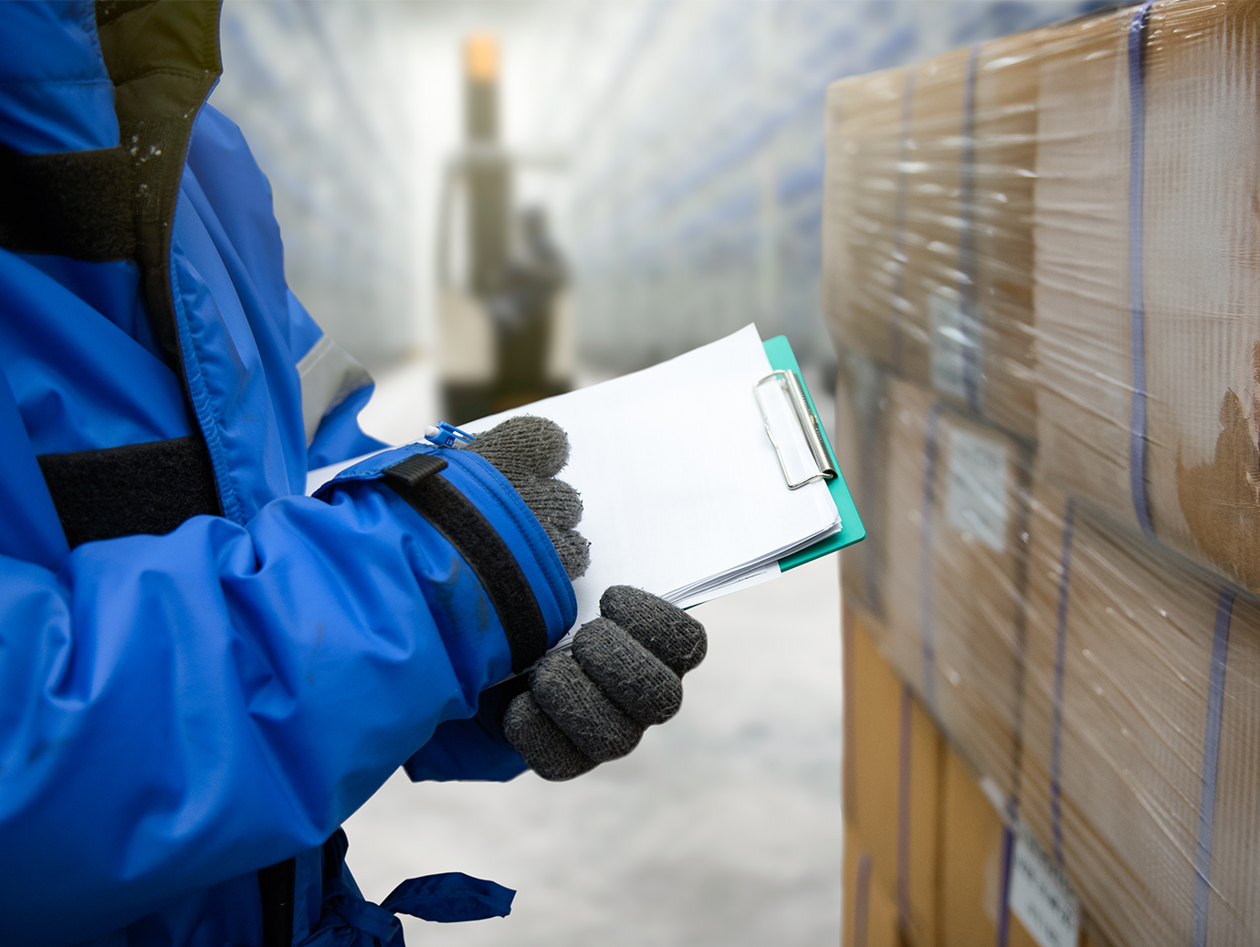Person in jackets holding a clipboard in front of cardboard boxes